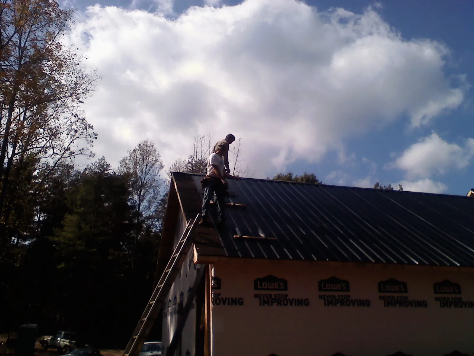 Roofer fastening dark metal panels high against a cloudy sky, from a Roof Inspection job in Toutle