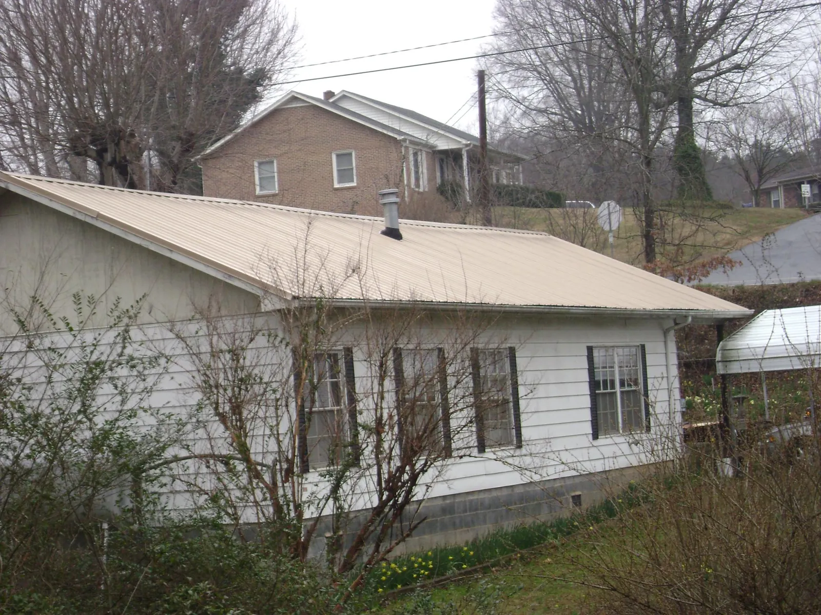 Tan metal roof on a white sided house set into a hillside — Commercial Roofing by Roofing Brothers in Toutle